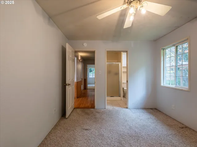 an empty room that has a chandelier fan and a window