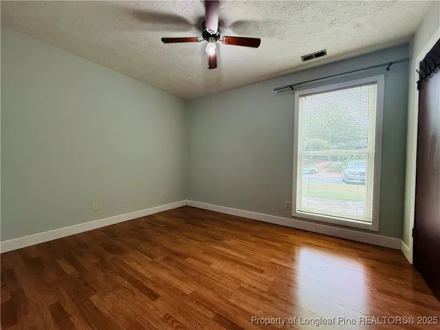 an empty room with wooden floor chandelier fan and windows