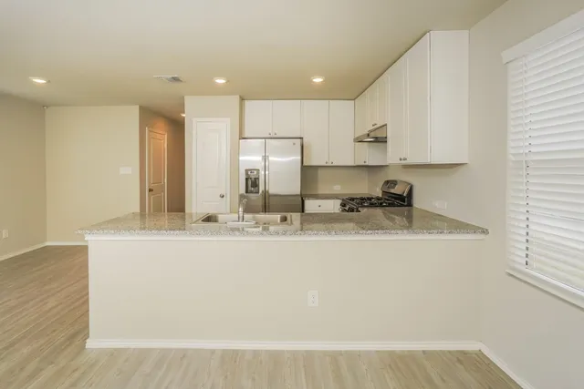 a view of kitchen with stainless steel appliances granite countertop a stove a sink a refrigerator and white cabinets with wooden floor