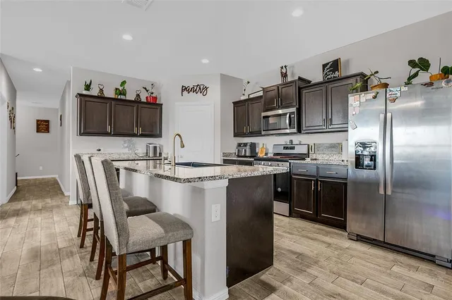 a kitchen with stainless steel appliances granite countertop a sink a stove a refrigerator and a dining table with wooden floor