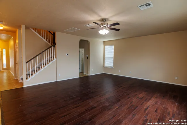 a view of an empty room with wooden floor and fan