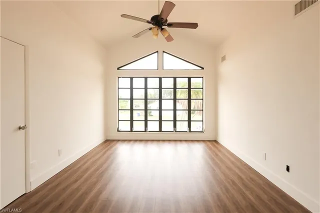 an empty room with wooden floor chandelier fan and windows