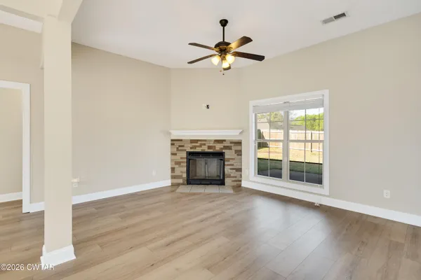 a view of an empty room with wooden floor fireplace and a window