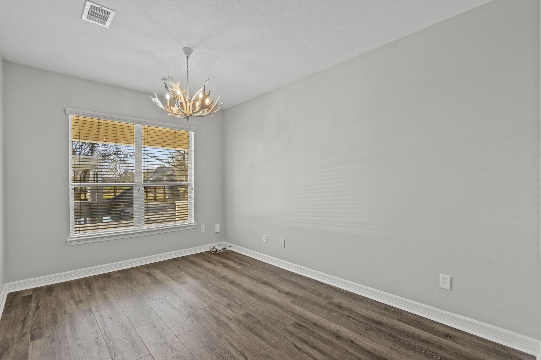 2730 Lawrence Road Kemah, TX 77565 - Photo 21 of 46 This room features a modern chandelier, large window with blinds offering natural light, and hardwood flooring. The light gray walls provide a neutral, versatile backdrop.