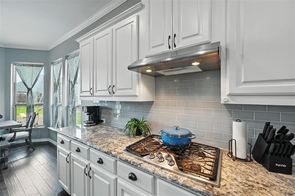 408 Mission Drive Forney, TX 75126 - Photo 12 of 40 Kitchen with under cabinet range hood, stainless steel gas stovetop, dark wood-type flooring, white cabinets, and decorative backsplash