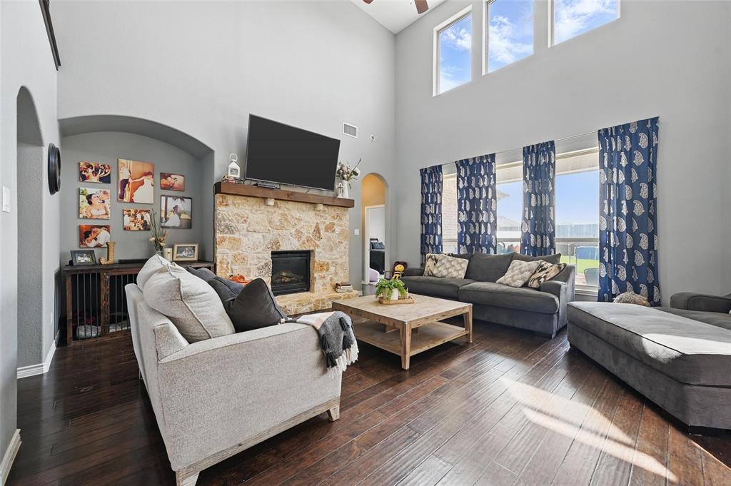 408 Mission Drive Forney, TX 75126 - Photo 4 of 40 Living room with arched walkways, a high ceiling, dark wood-style flooring, a ceiling fan, and a stone fireplace