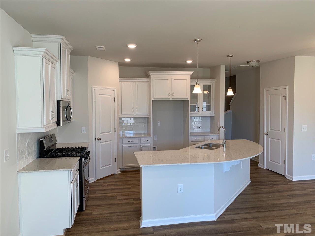 6108 Beale Loop, Unit 101 Raleigh, NC 27616 - Photo 3 of 30 a large kitchen with kitchen island a sink dishwasher a refrigerator and a stove with wooden floor