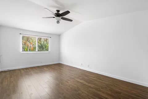 an empty room with wooden floor fan and windows