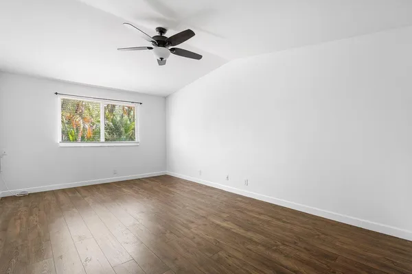 an empty room with wooden floor fan and windows