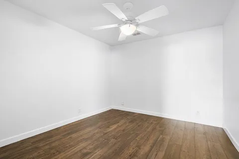 an empty room with wooden floor and fan