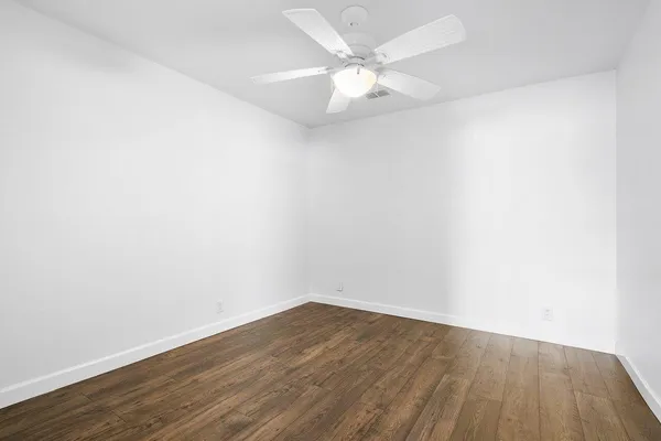 an empty room with wooden floor and fan