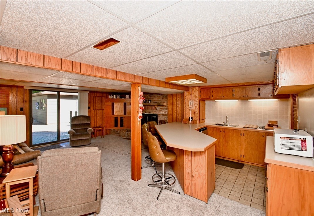5653 Dailey Road New Franklin, OH 44319 - Photo 10 of 24 Kitchen featuring a kitchen breakfast bar, a drop ceiling, light colored carpet, and wooden walls