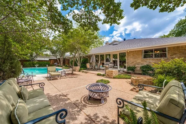 a view of a patio with couches table and chairs under an umbrella with large trees