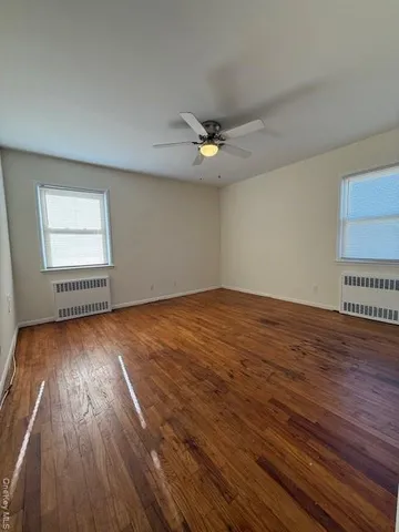 an empty room with wooden floor chandelier fan and windows