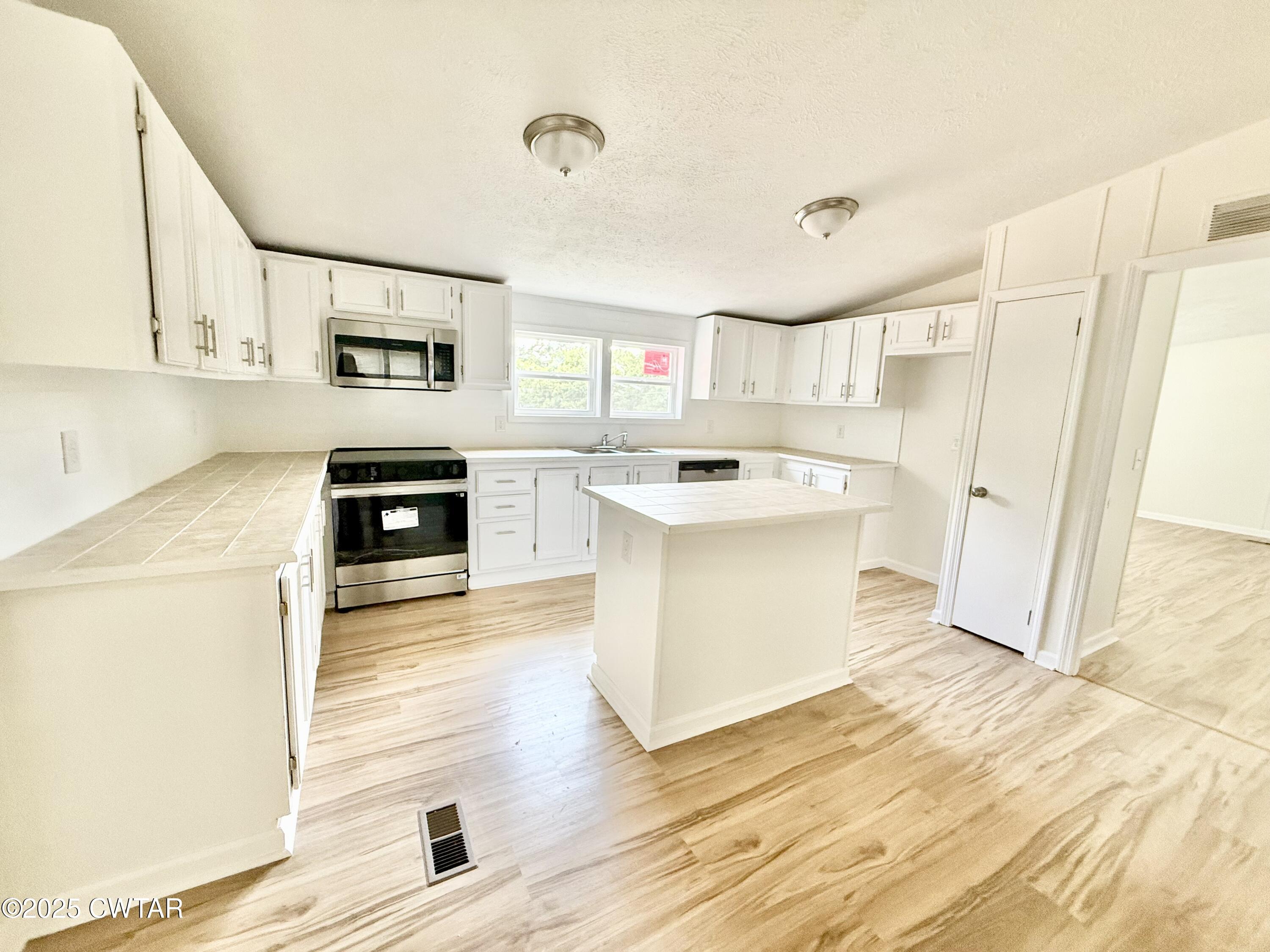390 Emerson Road Gates, TN 38037 - Photo 14 of 54 a kitchen with stainless steel appliances a stove top oven a sink a refrigerator white cabinets and wooden floor