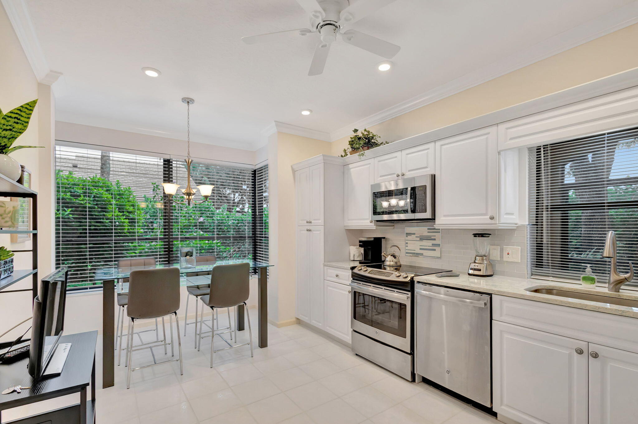 16151 West Bay Drive, Unit 161 Jupiter, FL 33477 - Photo 11 of 25 a kitchen with stainless steel appliances kitchen island granite countertop a stove a sink a refrigerator white cabinets and a dining table with garden view