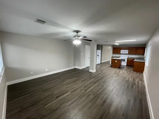 a view of an empty room with wooden floor and a ceiling fan