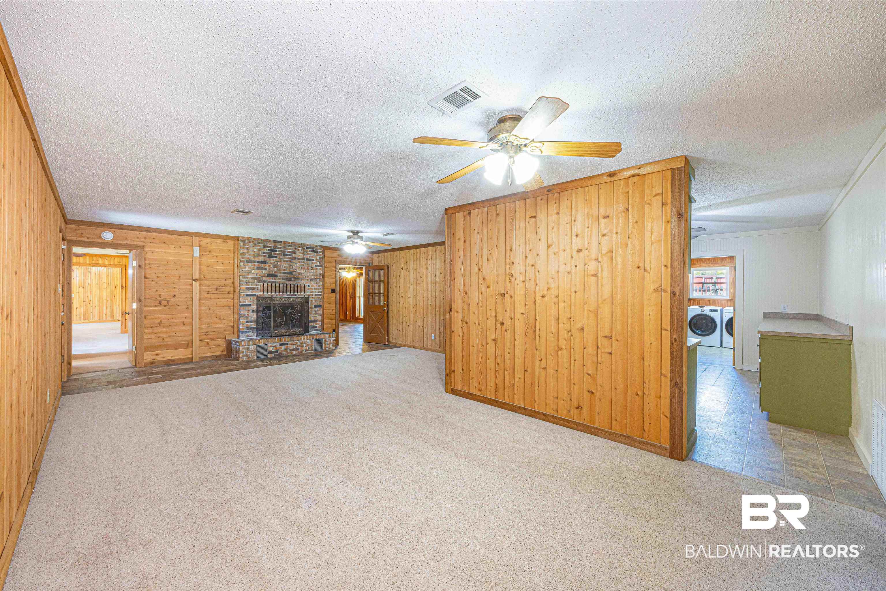 43101 Brown Road Bay Minette, AL 36507 - Photo 22 of 81 Unfurnished living room with light colored carpet, wooden walls, a brick fireplace, a textured ceiling, and washing machine and dryer