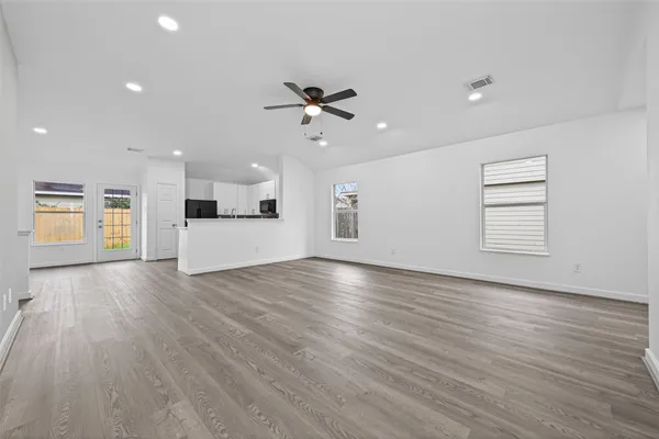 an empty room with wooden floor kitchen view and a window