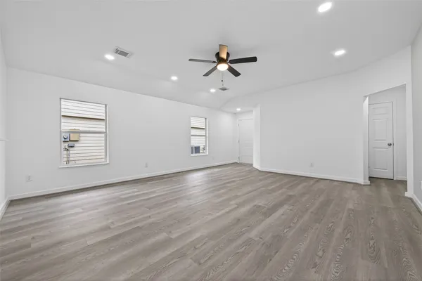an empty room with wooden floor ceiling fan and windows