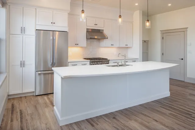 a kitchen with stainless steel appliances granite countertop a refrigerator a sink a stove and white cabinets with wooden floor