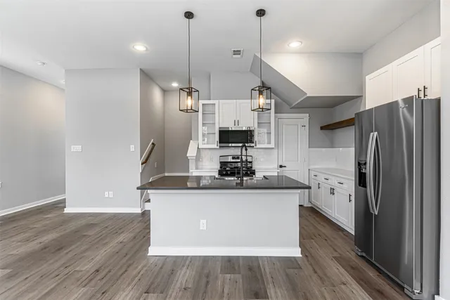 a kitchen with stainless steel appliances a refrigerator a sink dishwasher a stove and white cabinets with wooden floor