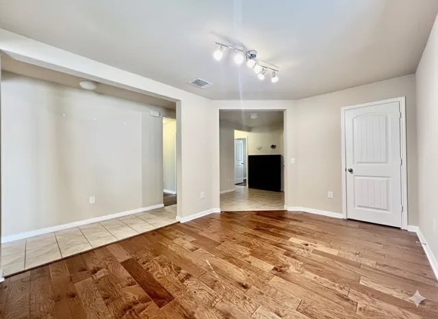 a view of an empty room with wooden floor and a kitchen