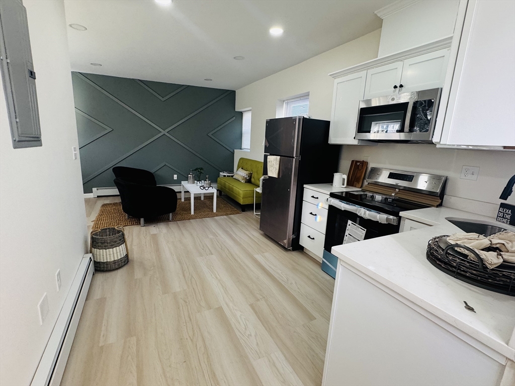 73 Victoria Street Revere, MA 02151 - Photo 4 of 24 a kitchen with stainless steel appliances a stove a refrigerator a sink a dining table and chairs with wooden floor