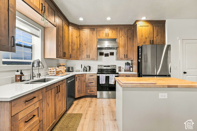 215 South Copper Road East Kanab, UT 84741 - Photo 9 of 41 Kitchen featuring custom wood cabinetry, stainless steel appliances, light-toned countertops, wood-finish flooring, and a center island with a butcher block top