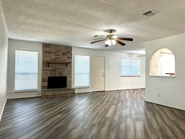 an empty room with wooden floor a ceiling fan a fireplace and windows