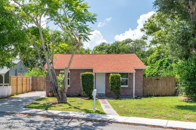 a view of a house with a yard plants and large tree