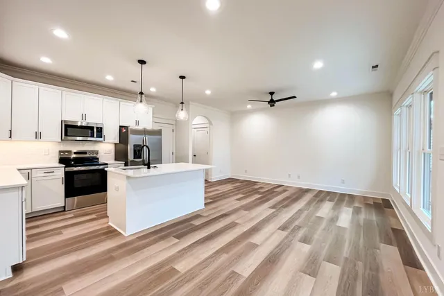 a large white kitchen with kitchen island a stove a sink dishwasher and white cabinets with wooden floor