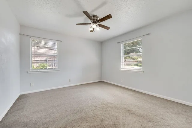 an empty room with ceiling fan and windows