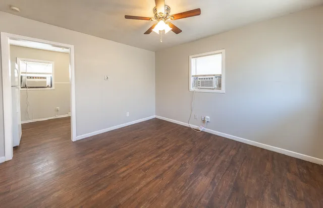 an empty room with wooden floor chandelier fan and windows