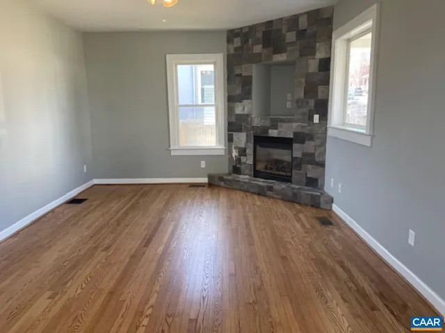 an empty room with wooden floor fireplace and windows