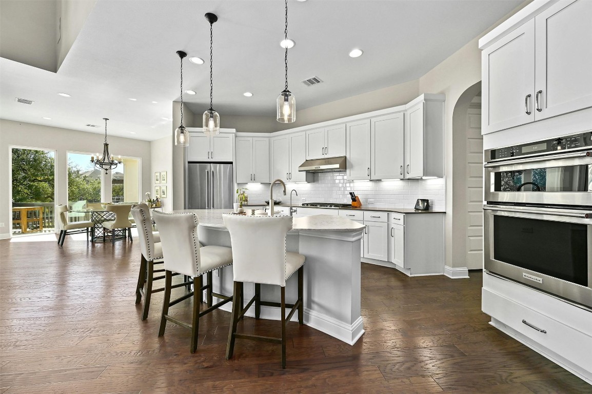 a kitchen with stainless steel appliances kitchen island granite countertop a stove a refrigerator a kitchen island a dining table and chairs with wooden floor