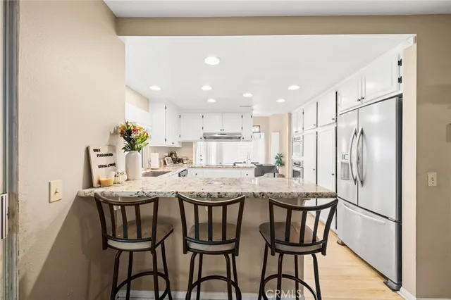 a room with stainless steel appliances kitchen island granite countertop a dining table chairs and a refrigerator