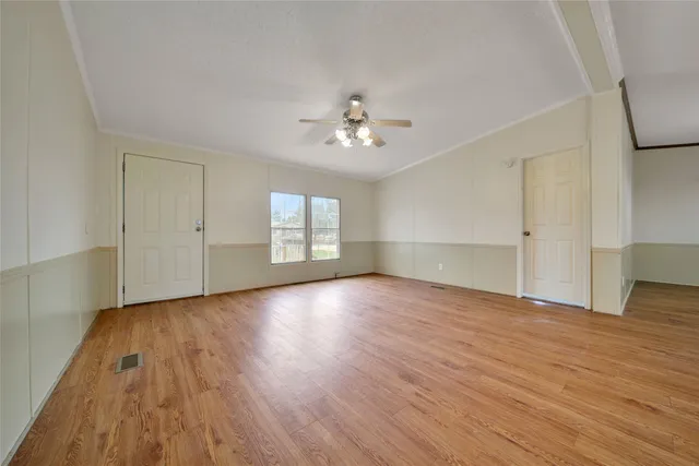 an empty room with wooden floor chandelier fan and windows