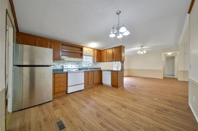 a kitchen with stainless steel appliances granite countertop a refrigerator a sink dishwasher a stove and a dining table with wooden floor