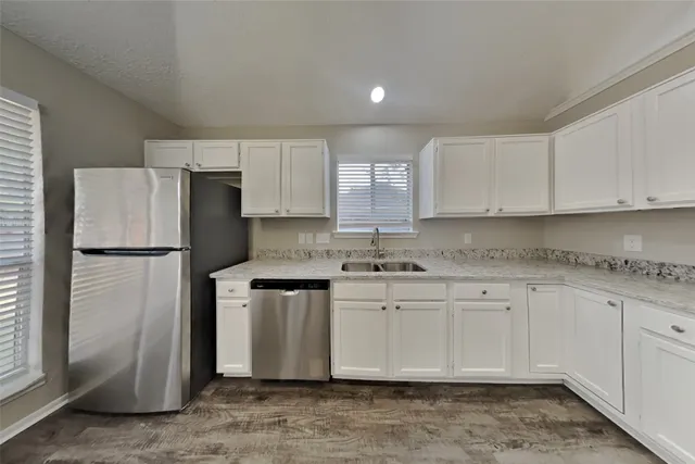 a kitchen with stainless steel appliances granite countertop a refrigerator a stove a sink and white cabinets