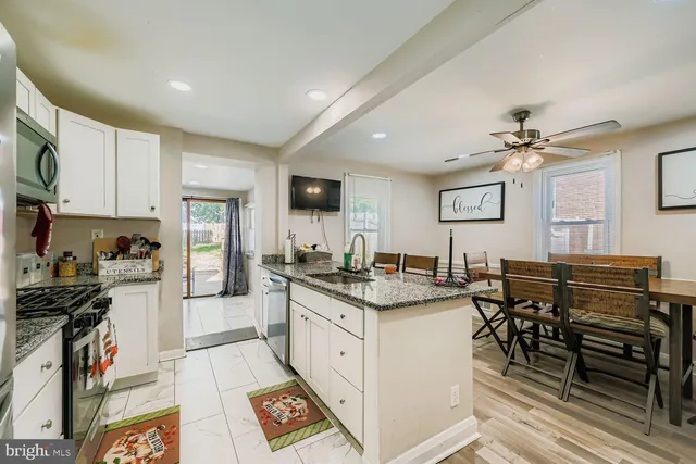 a kitchen with stainless steel appliances granite countertop a stove top oven a sink a dining table and chairs with white cabinets