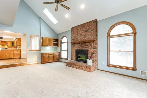 an empty room with windows fireplace and a kitchen view