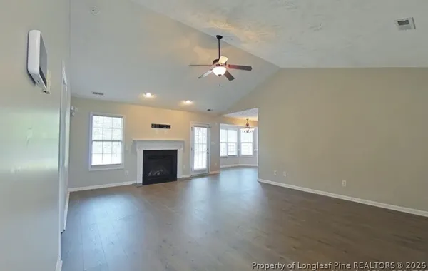 an empty room with windows fireplace and a kitchen view