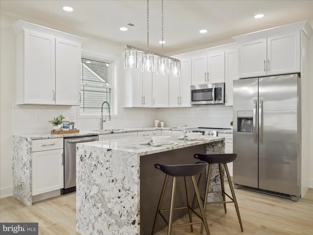 a kitchen with stainless steel appliances granite countertop a refrigerator a sink a stove a microwave and white cabinets with wooden floor