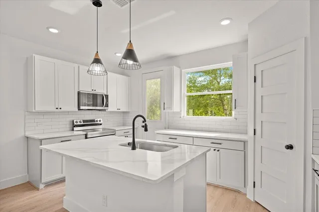 a kitchen with stainless steel appliances granite countertop a sink a window and white cabinets