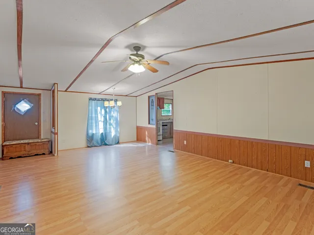 an empty room with wooden floor chandelier fan and windows