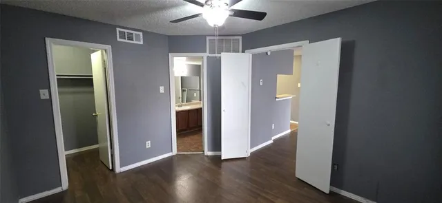 a view of an empty room with wooden floor and a ceiling fan