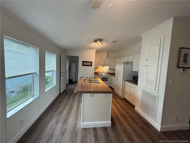 a large kitchen with a large window a refrigerator and a wooden floor