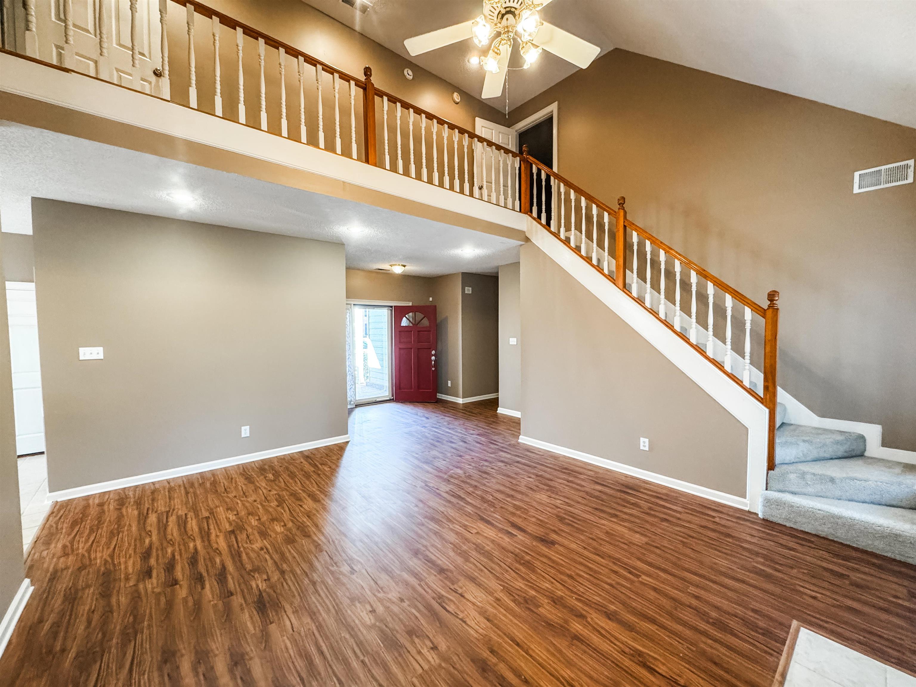 158 Eulas Ridge Cove Collierville, TN 38017 - Photo 4 of 18 Unfurnished living room with wood finished floors, visible vents, baseboards, high vaulted ceiling, and stairs