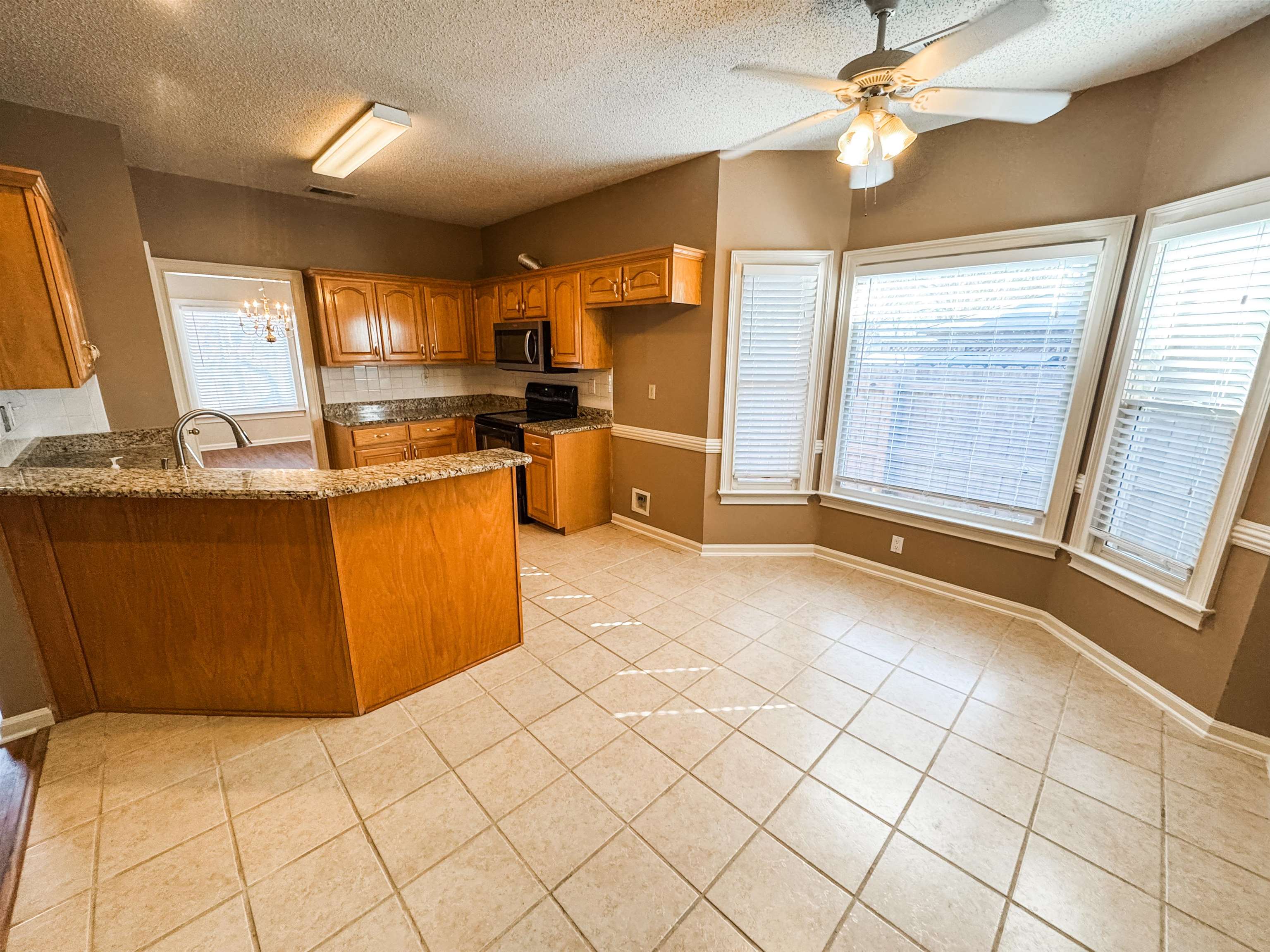 158 Eulas Ridge Cove Collierville, TN 38017 - Photo 5 of 18 Kitchen featuring light tile patterned floors, a peninsula, plenty of natural light, stainless steel microwave, and brown cabinets